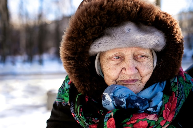 Oude trieste grootmoeder gewikkeld in een sjaal in de verte kijken