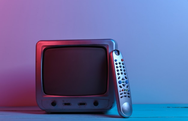 Oude tv-ontvanger met tv-afstandsbediening in rood blauw neonlicht. Retro golf, media