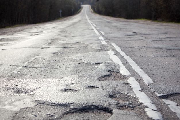 Oude versleten asfaltoppervlak op weg of snelweg na winterseizoen. Slechte weg met kuilen en gaten