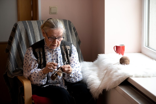 Oude vrouw aan het breien in een verpleeghuis bij het raam