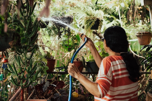 Oude vrouw die de tuin water geeft.