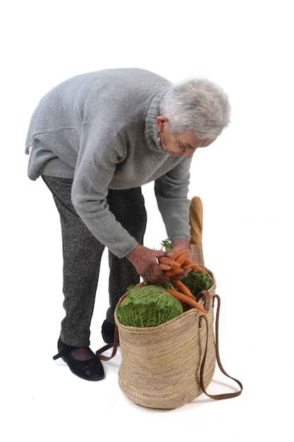 Oude vrouw die met een rieten mand gaat kopen die op wit wordt geïsoleerd