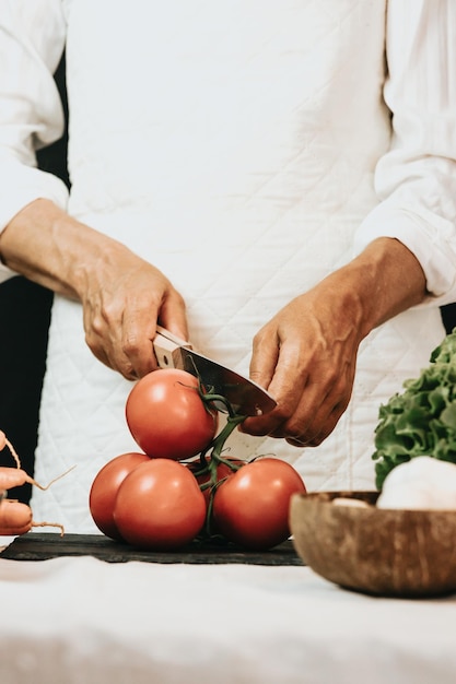 Oude vrouw die verse tomaten snijdt in de keukenclose-up die vers gezond voedsel met groenten voorbereidt rustieke keuken koken gemaakt door chef-kok voorbereiding van ingrediënt voor een biomaaltijd dieet en verzorgend voedsel