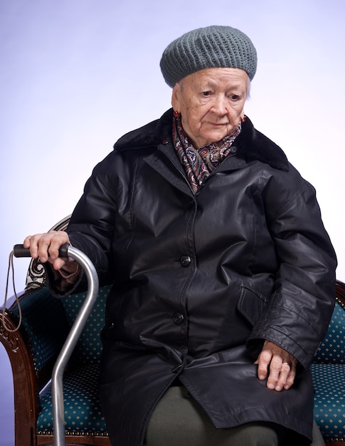 Oude vrouw met een stok in de winter uitloper zittend op een stoel