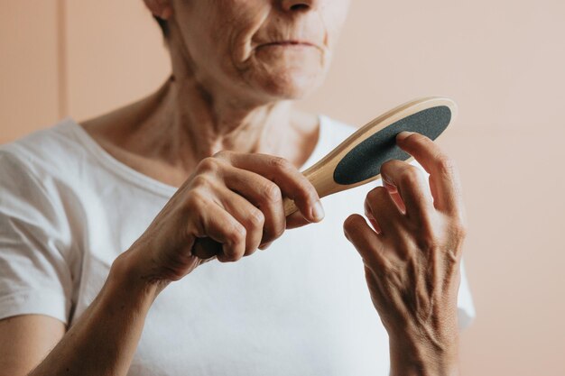 Oude vrouw vijlt haar nagels, verwijderbare vleeskleurige achtergrond. Oudere vrouw krijgt een manicure. Vrouw bereidt nagels voor op gellak, vijlt gel neer met filer. Een vrouw maakt haar eigen manicure.