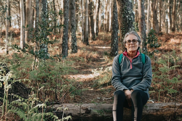 Foto oude vrouw zittend op een boomstam lachend in het bos tijdens een herfstdag met kopie ruimte