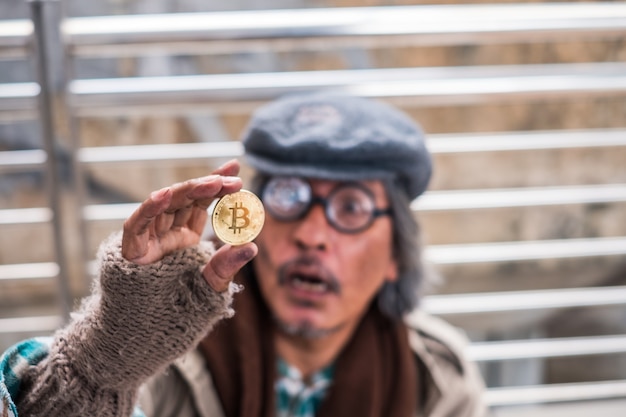 Oude vuile dakloze man die gouden bitcoin vasthoudt en er opgewonden uitziet