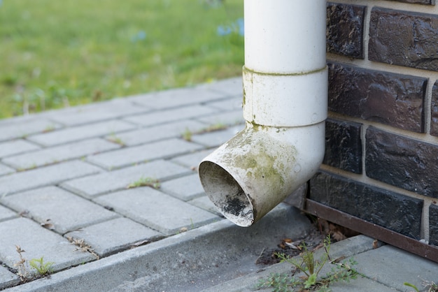 Oude witte plastic rioolbuis op de bruine bakstenen muur. Regenpijp