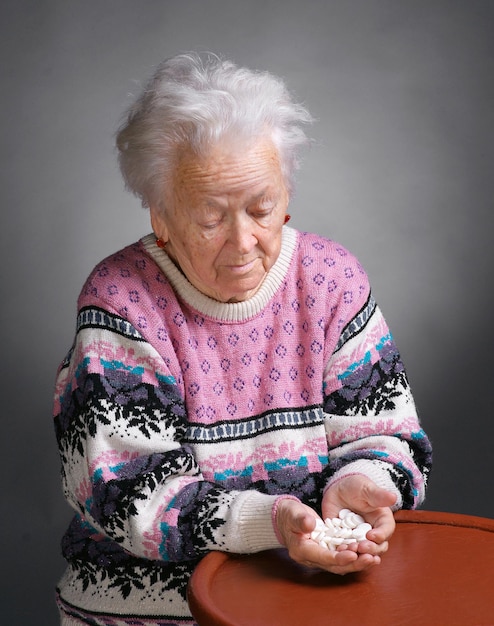 Oude zieke vrouw met pillen op een grijze achtergrond