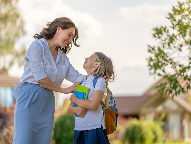 Ouder en leerling van de basisschool gaan hand in hand. Vrouw en meisje met rugzak achter de rug. Begin van de lessen.