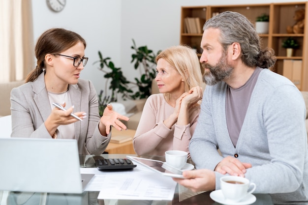 Ouder paar en makelaar zitten door tafel in de woonkamer en financiële punten bespreken