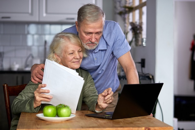 Ouder paar financiën thuis met behulp van laptop controleren, samen plannen van budget bespreken, met behulp van online bankdiensten en rekenmachine, documenten in de keuken houden