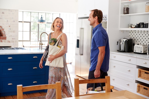 Foto ouder paar keert terug naar huis van een shoppingtrip met boodschappentassen door de keuken