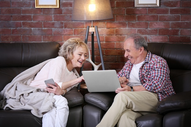 Ouder paar met behulp van laptop en mobiele telefoon samen thuis