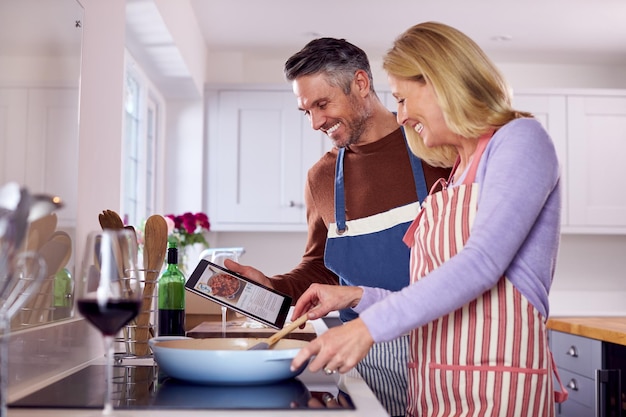 Ouder paar thuis volgens recept op digitale tablet in keuken terwijl ze samen de maaltijd bereiden