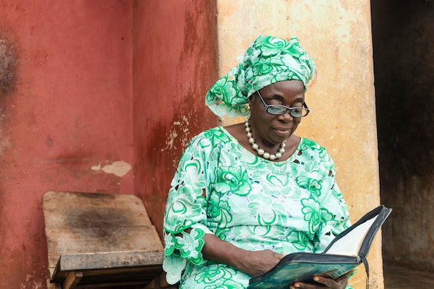 Oudere aantrekkelijke afrikaanse vrouw die terloops gekleed is in traditionele kleding die zich concentreert op het lezen van een boek