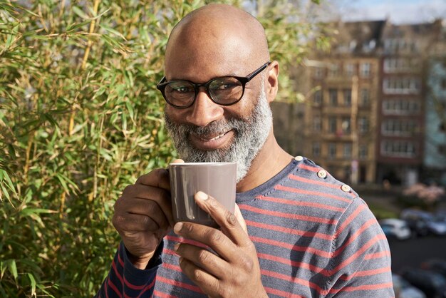 Oudere amn staat op het balkon en drinkt koffie