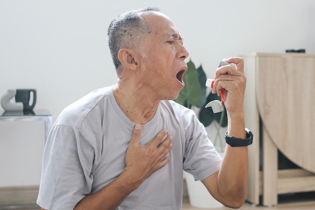 Foto oudere aziatische man gebruikt inhalator voor verlichting van een aanval thuis