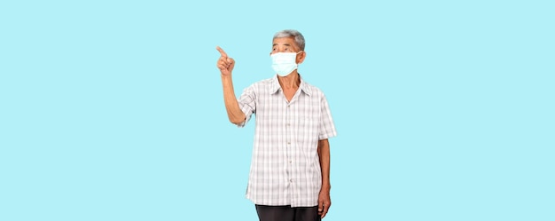 Oudere Aziatische man met een masker is ziek Wijzende vinger geïsoleerd op een blauwe achtergrond in de studio