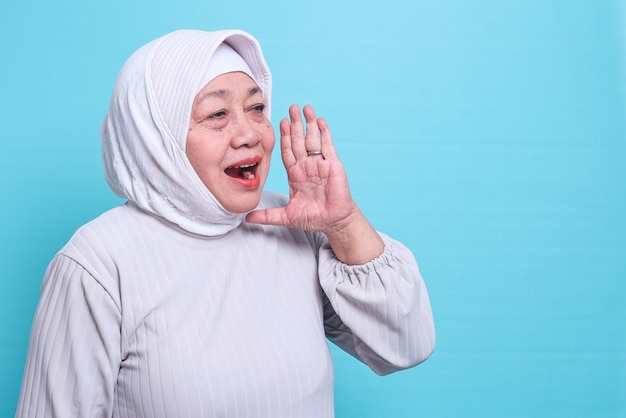 Oudere Aziatische moslimvrouw met een hoofddoek die luid schreeuwt met een hand op haar mond