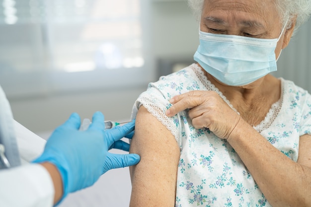 Oudere aziatische senior vrouw met gezichtsmasker die covid19 of coronavirusvaccin krijgt