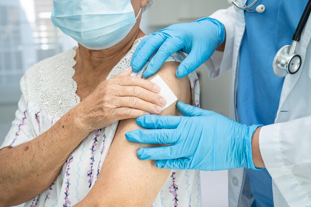 Oudere Aziatische seniorvrouw die een gezichtsmasker draagt en door een arts een injectie van het COVID-19 of coronavirusvaccin krijgt