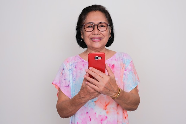 Oudere Aziatische vrouw glimlacht en kijkt naar de camera terwijl ze een mobiele telefoon vasthoudt