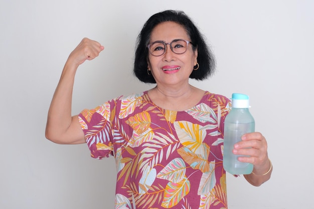 Oudere Aziatische vrouw glimlacht en toont haar biceps terwijl ze een drinkfles vasthoudt