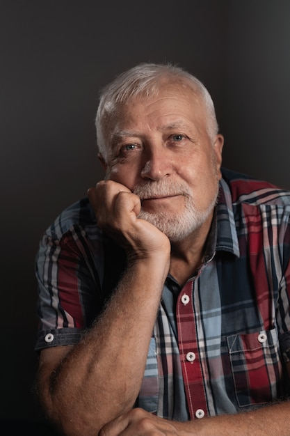 Foto oudere charismatische man steunde zijn hoofd op zijn hand, glimlachend kijkend naar de camera, portret