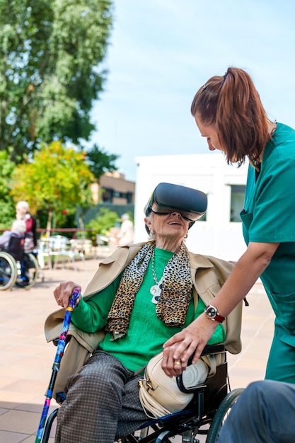 Oudere dame in rolstoel probeert VR met de hulp van een verpleegster op de patio van een verzorgingshuis