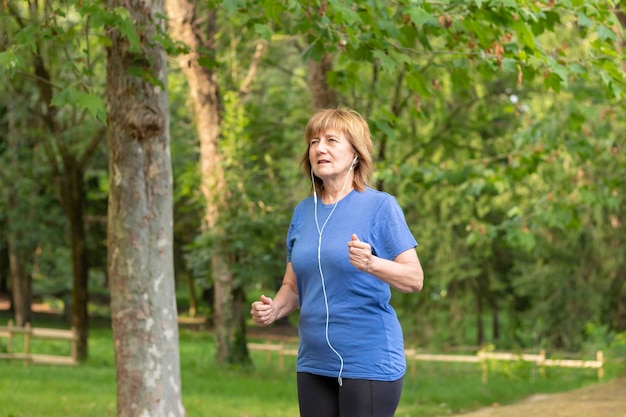 Oudere dame loopt door de natuur in sportkleding terwijl ze naar muziek luistert met een koptelefoon