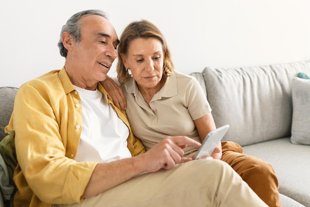 Oudere echtgenoten die mobiel surfen op internet of videobellen terwijl het gezin op de bank zit