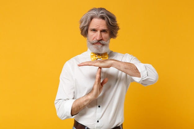 Oudere grijsharige snor bebaarde man in wit overhemd vlinderdas poseren geïsoleerd op geel oranje muur achtergrond in studio. Mensen levensstijl concept. Bespotten kopie ruimte. Handen loodrecht vasthouden.