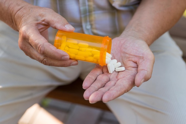 Oudere hand houdt pillen vast oranje tabletcontainer nieuw type antibiotica medicijn dat pijn onderdrukt