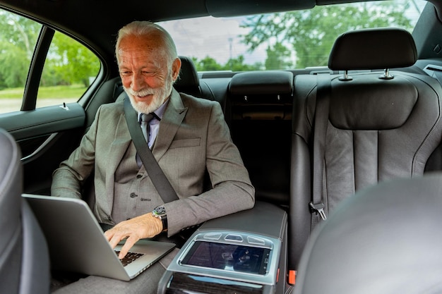 Oudere heer die aandachtig schrijft op laptop in het comfort van zijn auto