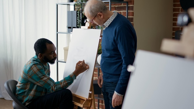 Oudere kunstenaar die kunstleerling nieuwe tekentechniek leert om te helpen bij educatieve ontwikkeling en groei. Creatieve persoon die artistiek advies krijgt van senior man om meesterwerk te tekenen.