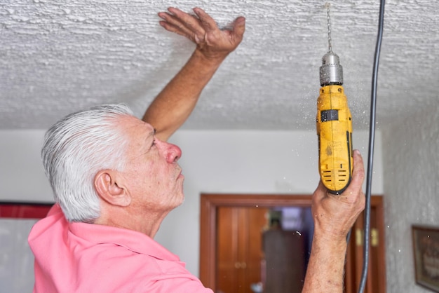 Foto oudere man die bouwwerk doet in zijn huis met een boor