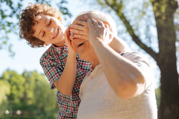 Oudere man die een glimlach op zijn gezicht houdt en in semi-positie staat terwijl hij een weekend doorbrengt op de natuur