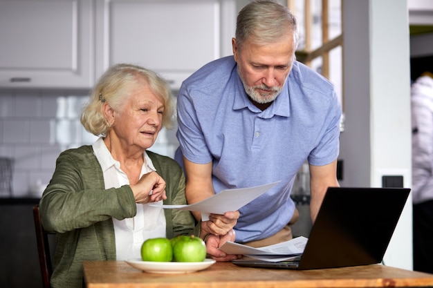 oudere man en vrouw beheren maandelijks gezinsbudget samen, gericht getrouwd stel met behulp van computerbankieren, rekeningen tellen in de keuken