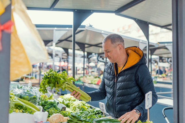 Oudere man groenten plukken op boerenmarkt.