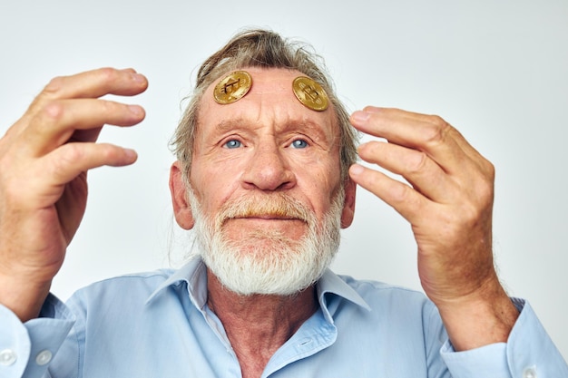 Oudere man in een blauw shirt bitcoins op het gezicht geïsoleerde achtergrond