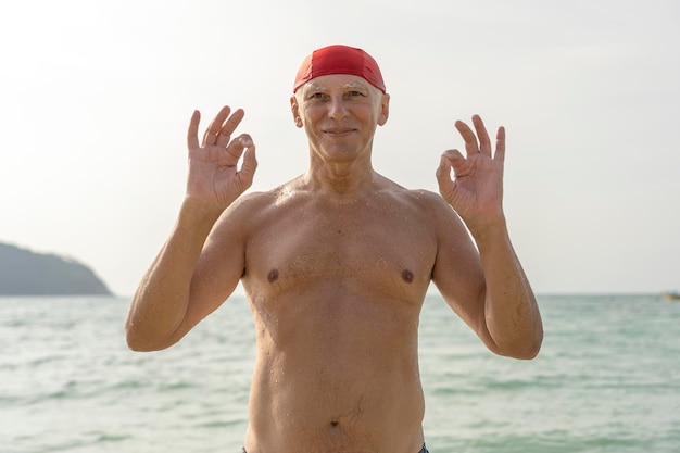 Oudere man in een rode zwemhoed op het strand bij het zeewater