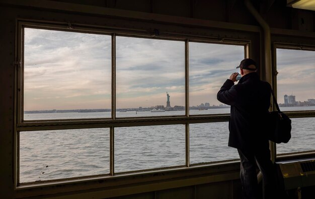 Oudere man maakt een foto met zijn smartphone vanaf de boot die het vrijheidsbeeld in New Yo . bezoekt