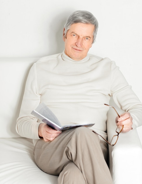 Oudere man met digitale tablet zittend in een stoel. Geïsoleerd op witte muur