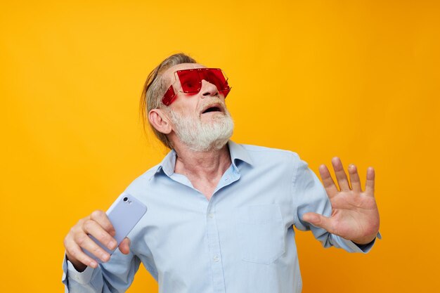 Foto oudere man met een mobiele telefoon die tegen een gele achtergrond gebaren maakt