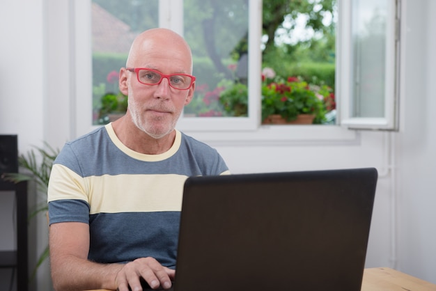 Oudere man met laptop in zijn huis