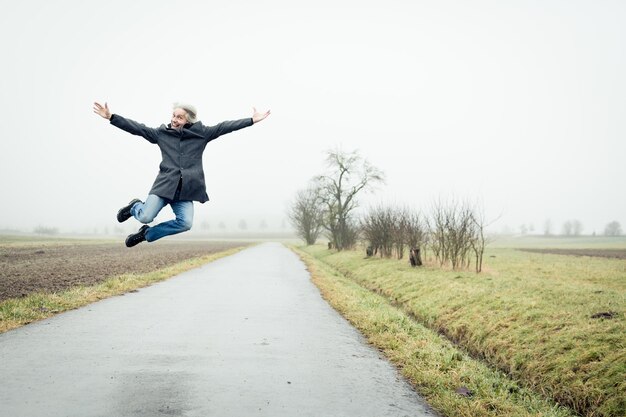 Foto oudere man springt op de weg tegen de lucht tijdens mistig weer