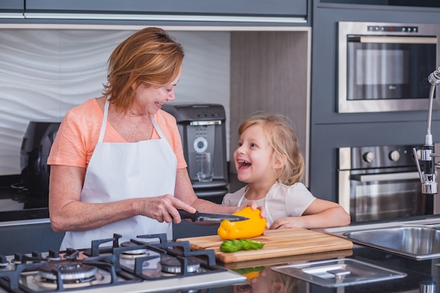 Oudere moeder en dochtertje samen koken. Moeder en dochter snijden groenten om te koken