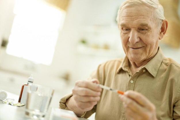 Oudere opa bestudeert een medische spuit in zijn handen