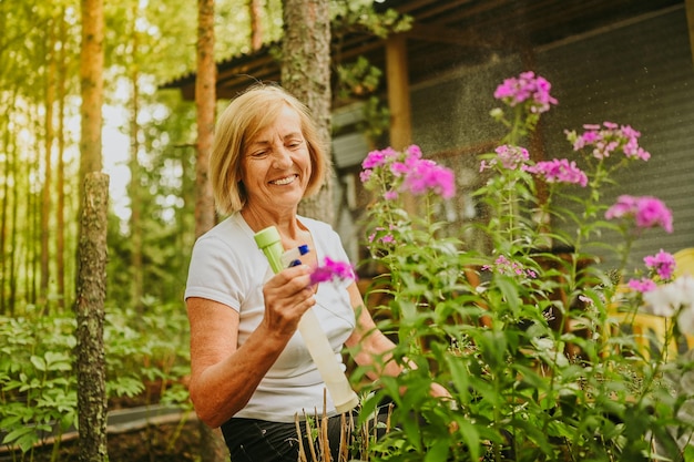 Oudere senior tuinman boer vrouw zorgzame bloemen in de zomertuin op het platteland buitenshuis sprays